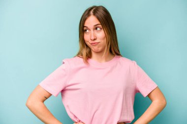 Kafkasyalı genç bir kadın mavi arka planda izole edilmiş, kafası karışmış, şüpheli ve kendinden emin değil..