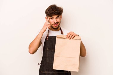 Beyaz arka planda izole edilmiş bir çanta taşıyan genç İspanyol tezgahtar işaret parmağıyla hayal kırıklığı jesti gösteriyor..