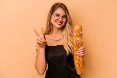 Beyaz tenli fırıncı kadın bej arka planda izole edilmiş. İki numarayı parmaklarıyla gösteriyor..
