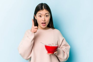 Mavi arka planda bir kase mısır gevreği tutan genç Asyalı kadının bir fikri var, ilham verici bir kavram..