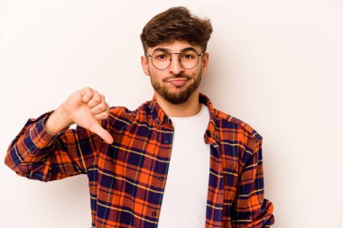 Beyaz arka planda izole edilmiş genç İspanyol adam baş parmağını aşağı gösteriyor, hayal kırıklığı konsepti..