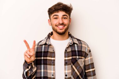 Beyaz arka planda izole edilmiş genç İspanyol adam zafer işareti gösteriyor ve gülümsüyor..