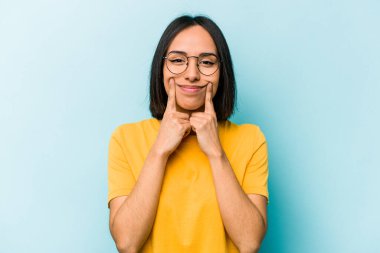 Mavi arka planda izole edilmiş genç İspanyol kadın iki seçenek arasında şüphe duyuyor.