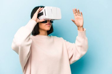 Mavi arka planda izole edilmiş sanal gözlük takan genç İspanyol kadın.