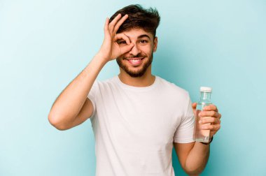 Beyaz arka planda izole edilmiş bir şişe su tutan İspanyol genç adam heyecanlı..