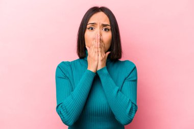 Pembe arka planda izole edilmiş genç İspanyol kadın elleri endişeli bir şekilde ağzı örtüyor..