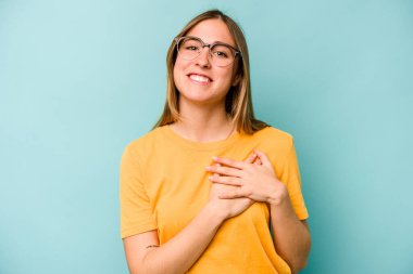 Mavi arka planda soyutlanmış genç beyaz kadın gülüyor, elini yüreğine koyuyor, mutluluk kavramını koruyor..