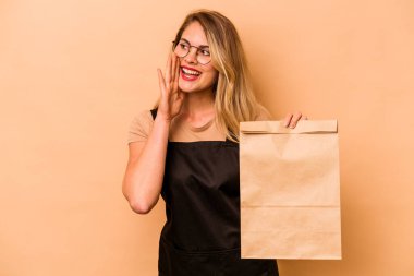 Restoran garsonu, elinde bej arka planda izole edilmiş paket taşıyan beyaz kadın bağırıyor ve ağzı açık bir şekilde avuç içini tutuyor..
