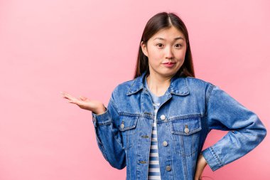 Pembe arka planda izole edilmiş genç Çinli bir kadın avucunun içinde bir fotokopi alanı olduğunu ve elini belinde tuttuğunu gösteriyor..