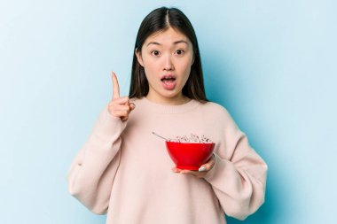 Mavi arka planda bir kase mısır gevreği tutan genç Asyalı kadının harika bir fikri var, yaratıcılık kavramı..