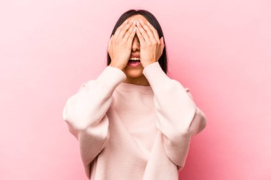 Pembe arka planda izole edilmiş genç İspanyol kadın yüzünün yarısını avuç içiyle kaplayarak eğleniyor..