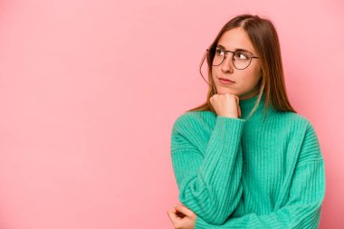 Pembe arka planda soyutlanmış beyaz bir kadın şüpheli ve şüpheci bir ifadeyle yana bakıyor..