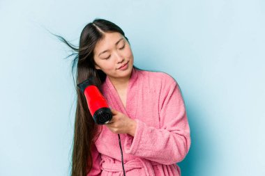 Mavi arka planda saç kurutan Asyalı genç kadın.