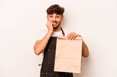 Beyaz arka planda izole edilmiş, tırnak yiyen, gergin ve endişeli bir çanta taşıyan genç İspanyol tezgahtar..