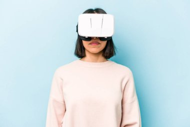 Mavi arka planda izole edilmiş sanal gözlük takan genç İspanyol kadın.