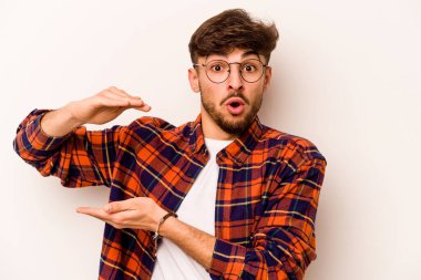 Beyaz arka planda izole edilmiş genç İspanyol adam iki eliyle bir şey tutuyor, ürün sunumu..