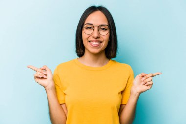 Mavi arka planda izole edilmiş genç İspanyol kadın farklı kopya alanlarını gösteriyor, birini seçiyor, parmaklarıyla gösteriyor..