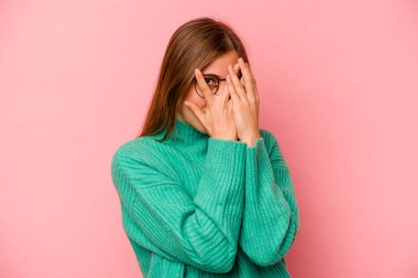 Pembe arka planda izole edilmiş genç beyaz kadın parmaklarıyla gözünü kırp korkmuş ve gergin..