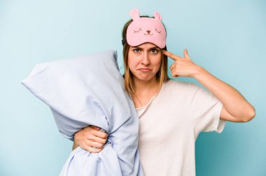 Mavi arka planda izole edilmiş pijama giyen beyaz bir kadın işaret parmağıyla yaptığı hayal kırıklığı jestini gösteriyor..