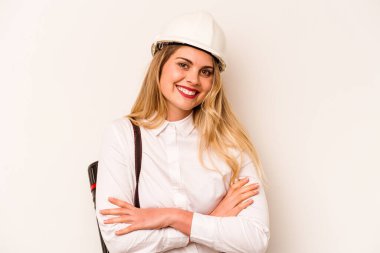 Miğferli ve elinde planları olan genç bir mimar kadın beyaz arka planda izole edilmiş gülüyor ve eğleniyor..