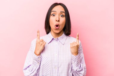 Pembe arka planda izole edilmiş, ağzı açık, üst tarafı işaret eden genç İspanyol kadın..