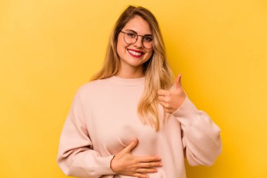 Sarı arka planda izole edilmiş genç beyaz kadın karnına dokunuyor, nazikçe gülümsüyor, yemek yiyor ve tatmin oluyor..