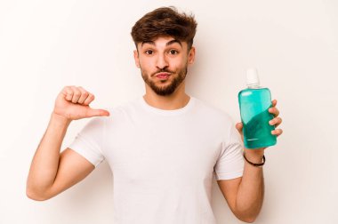 Young hispanic man holding mouthwash isolated on white background feels proud and self confident, example to follow.