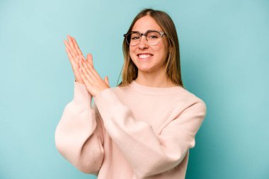 Mavi arka planda izole edilmiş genç beyaz kadın enerjik ve rahat hissediyor, ellerini ovuşturuyor..