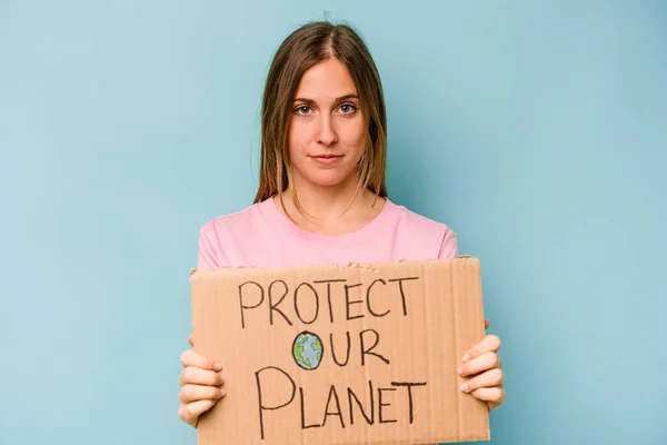 年轻的高加索女人拿着保护你的星球的标语牌被蓝色背景隔离 — 图库照片
