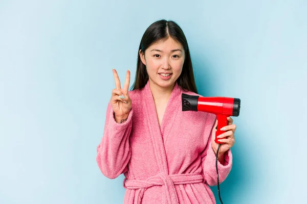 年轻的亚洲女人穿着浴衣 拿着用粉红背景隔开的吹风机 手指头伸出二号 — 图库照片