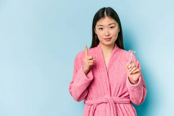 年轻的亚洲女人带着剃须刀刀片 蓝色背景显示第一手指 — 图库照片