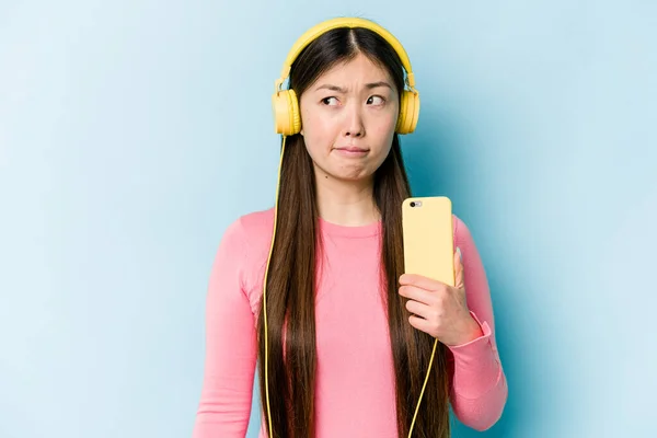 Jovem Mulher Asiática Ouvindo Música Isolada Fundo Azul Confuso Sente — Fotografia de Stock