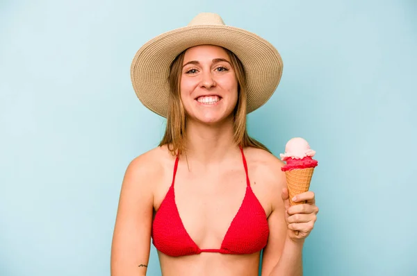 年轻的高加索女人穿着比基尼 手里拿着一个被蓝色背景隔开的冰淇淋 玩得很开心 — 图库照片