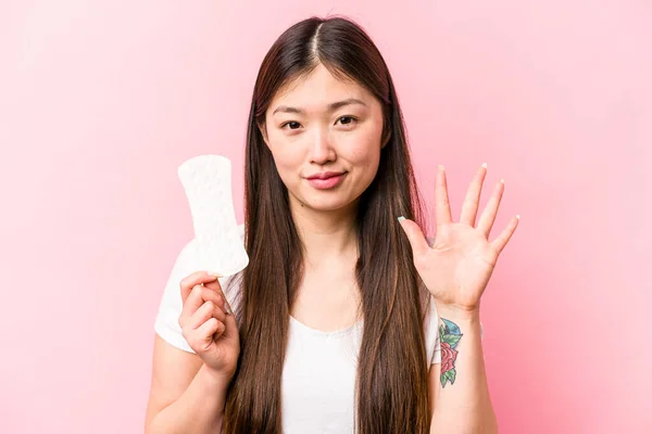 年轻的亚洲女人拿着卫生巾 带着粉红的背景 开开朗地微笑着 用手指拿着5号卫生巾 — 图库照片