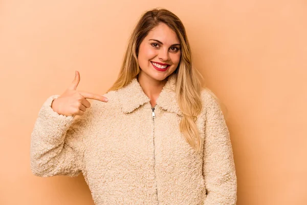 Beyaz tenli genç bir kadın, bej arka planda izole edilmiş. Gömlek fotokopisini elle gösteriyor. Gururlu ve kendinden emin.