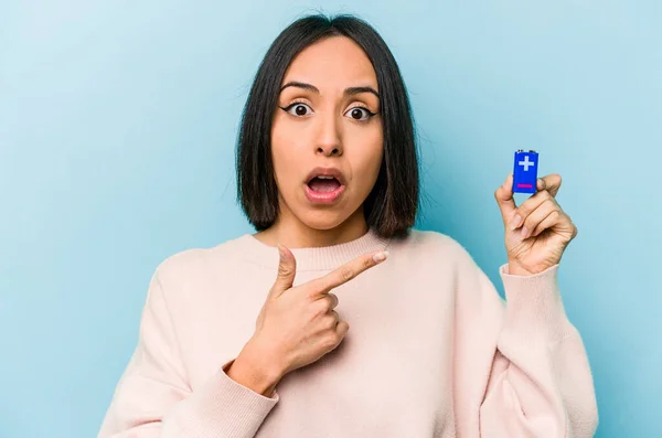 若いヒスパニック系の女性は 側を指して青色の背景に分離電池を保持 — ストック写真