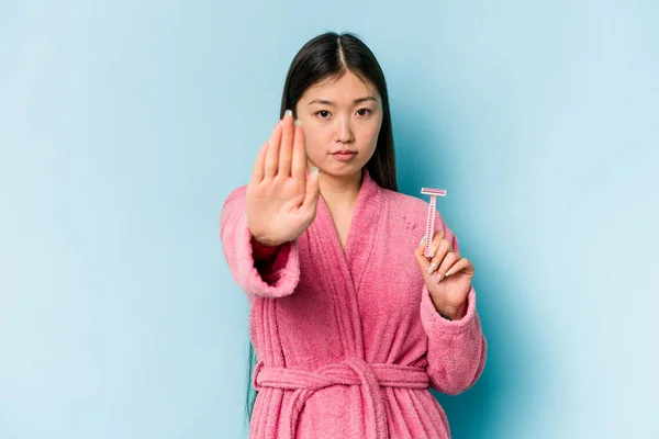 年轻的亚洲女人拿着剃须刀刀片 隔离在蓝色的背景上 伸出的手显示出停止的迹象 阻止了你 — 图库照片