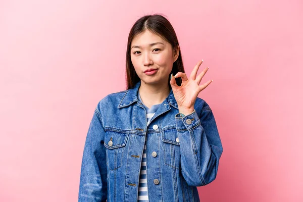被粉色背景隔离的年轻中国女人眨了眨眼 用手握住一个好的手势 — 图库照片