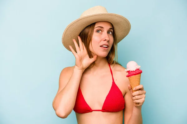 若いですCaucasian女性を身に着けていますビキニと持っていますアイスクリーム隔離上の青の背景に聞きしようとしているゴシップ — ストック写真
