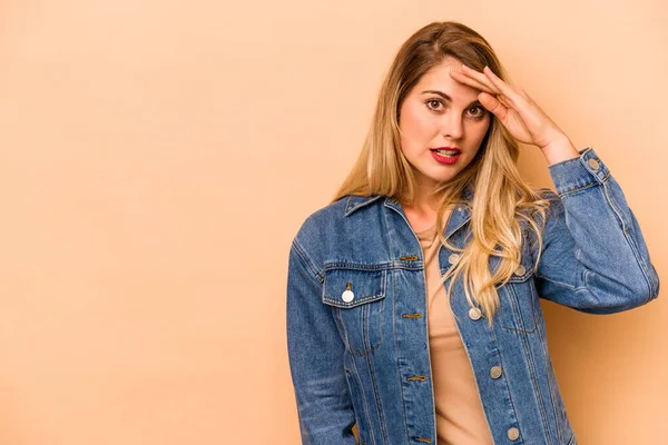 Beyazlı genç bir kadın bej arka planda izole edilmiş, uzaklara bakıyor ve elini alnına koyuyor..