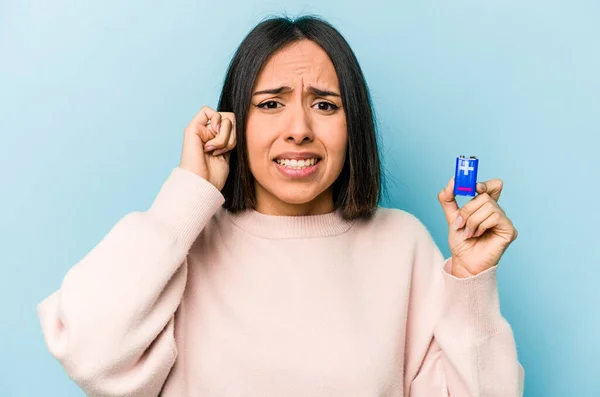Mladá Hispánská Žena Drží Baterie Izolované Modrém Pozadí Zakrývající Uši — Stock fotografie