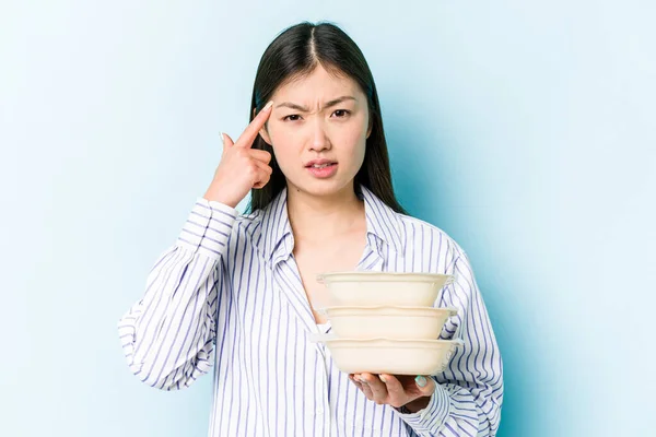年轻的亚洲女人拿着蓝色背景的Tupperware 用食指表现出失望的姿态 — 图库照片