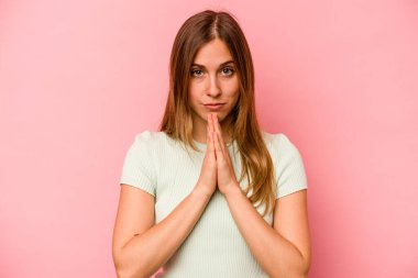 Pembe arka planda izole edilmiş genç beyaz kadın dua ediyor, bağlılık gösteriyor, dindar biri ilahi ilham arıyor..