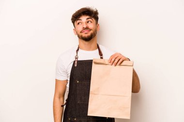 Genç İspanyol tezgahtar beyaz arka planda izole edilmiş bir çanta tutuyor. Amaçlarına ve amaçlarına ulaşmayı hayal ediyor.