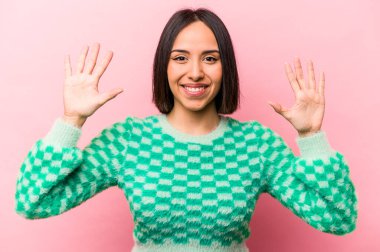 Pembe arka planda izole edilmiş genç İspanyol kadın on numarayı elleriyle gösteriyor..