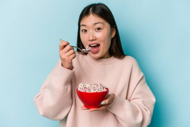 Genç Asyalı bir kadın mavi arka planda bir kase mısır gevreği tutuyor.