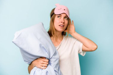 Mavi arka planda izole edilmiş pijama giyen beyaz bir kadın bir dedikoduyu dinlemeye çalışıyor..
