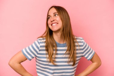 Pembe arka planda izole edilmiş genç beyaz kadın mutlu bir şekilde gülüyor ve ellerini karnının üstünde tutarak eğleniyor..