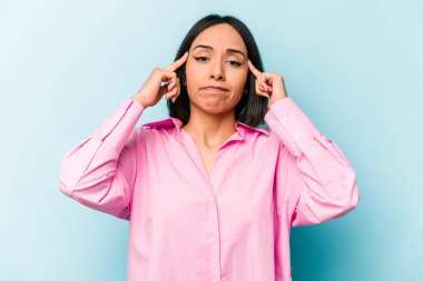 Mavi arka planda izole edilmiş genç İspanyol kadın bir işe odaklanmış, işaret parmaklarını işaret ediyor..