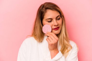 Pembe arka planda yüz süngeri tutan beyaz bir kadın var.